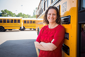woman smiling in front of school busses