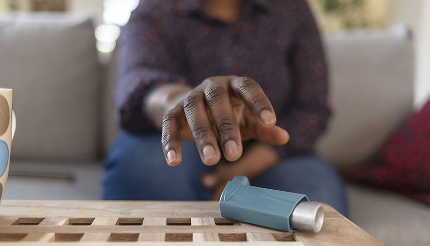 A hand reaching for an asthma inhaler on a table