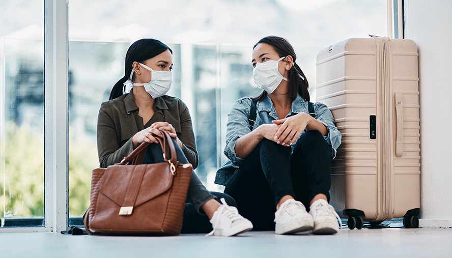 Two women sitting at the airport wearing facemasks