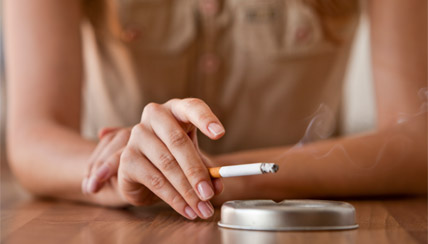 adult holding a cigarette over an ash tray
