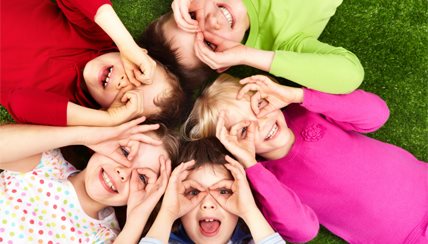 Kids making glasses with their hand laying in the grass