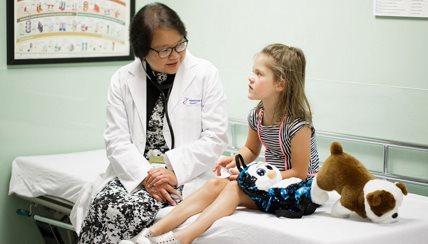 Doctor and child talking on hospital bed. The child has two stuffed animals