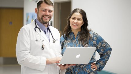 Two doctors smiling at the camera while holding a laptop