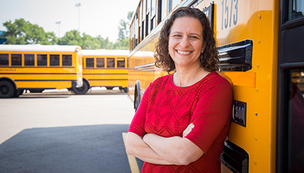 woman smiling in front of school busses